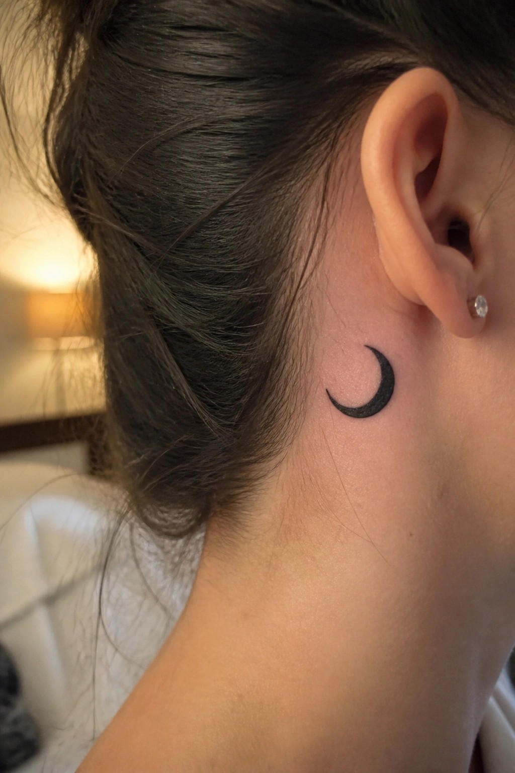 Dark hair in a bun with black crescent moon tattoo behind the ear