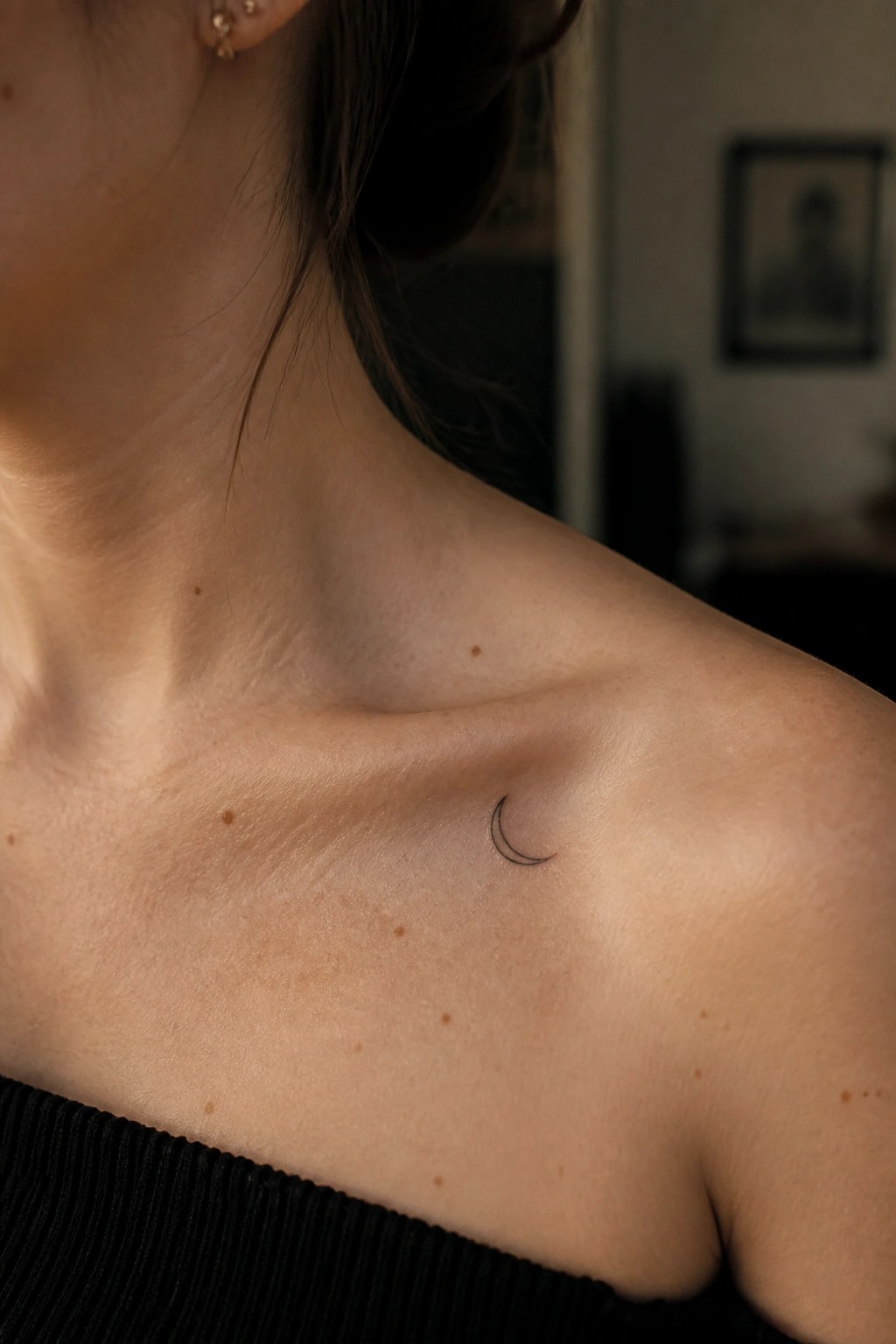 Freckled shoulder with small crescent moon tattoo, black off-shoulder top visible.