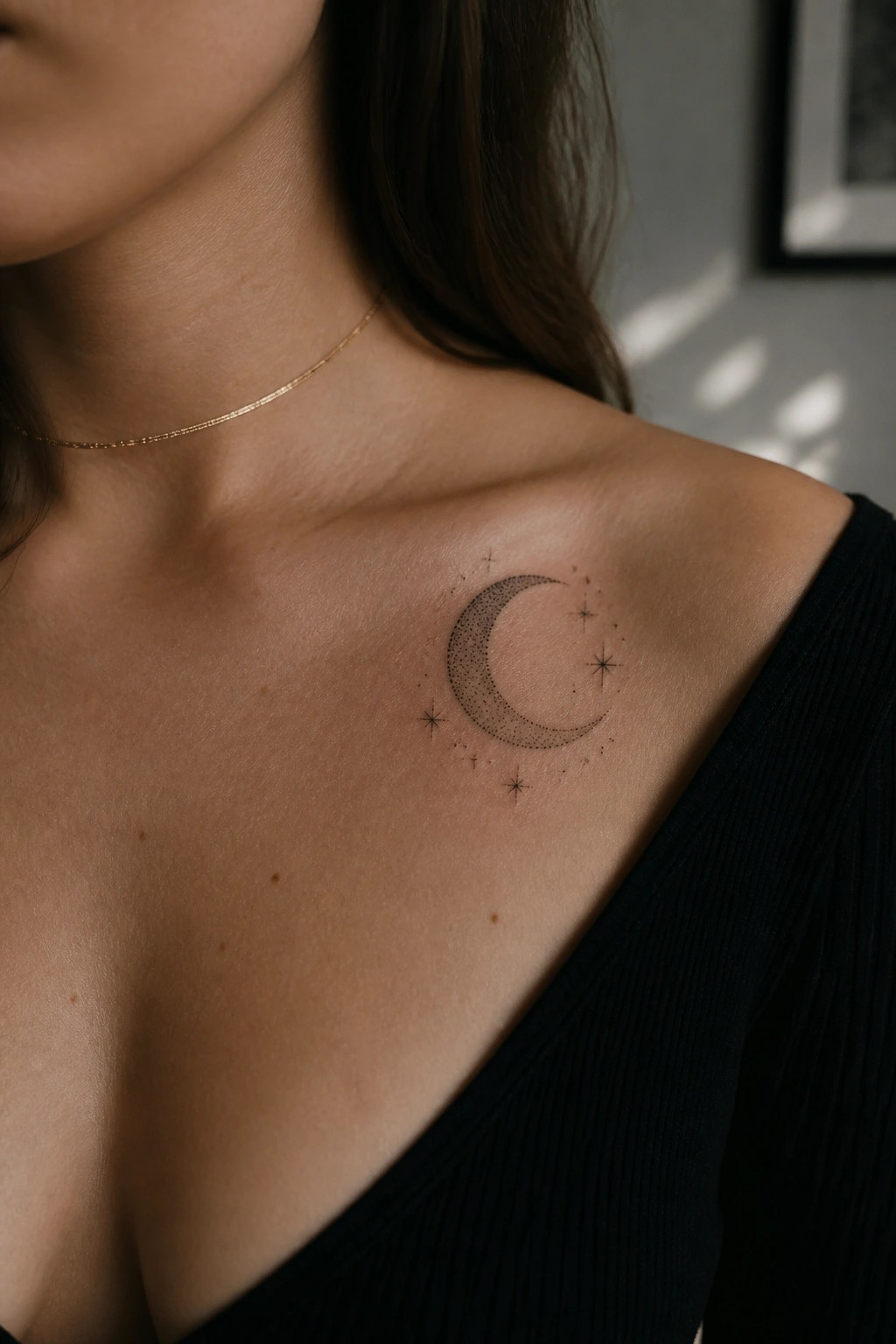 Woman's collarbone with crescent moon stars tattoo, gold necklace, black V-neck top