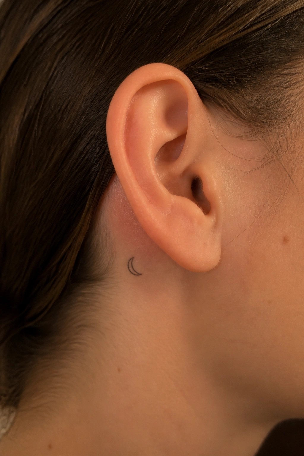 Close-up of an ear with a small crescent moon tattoo behind it.