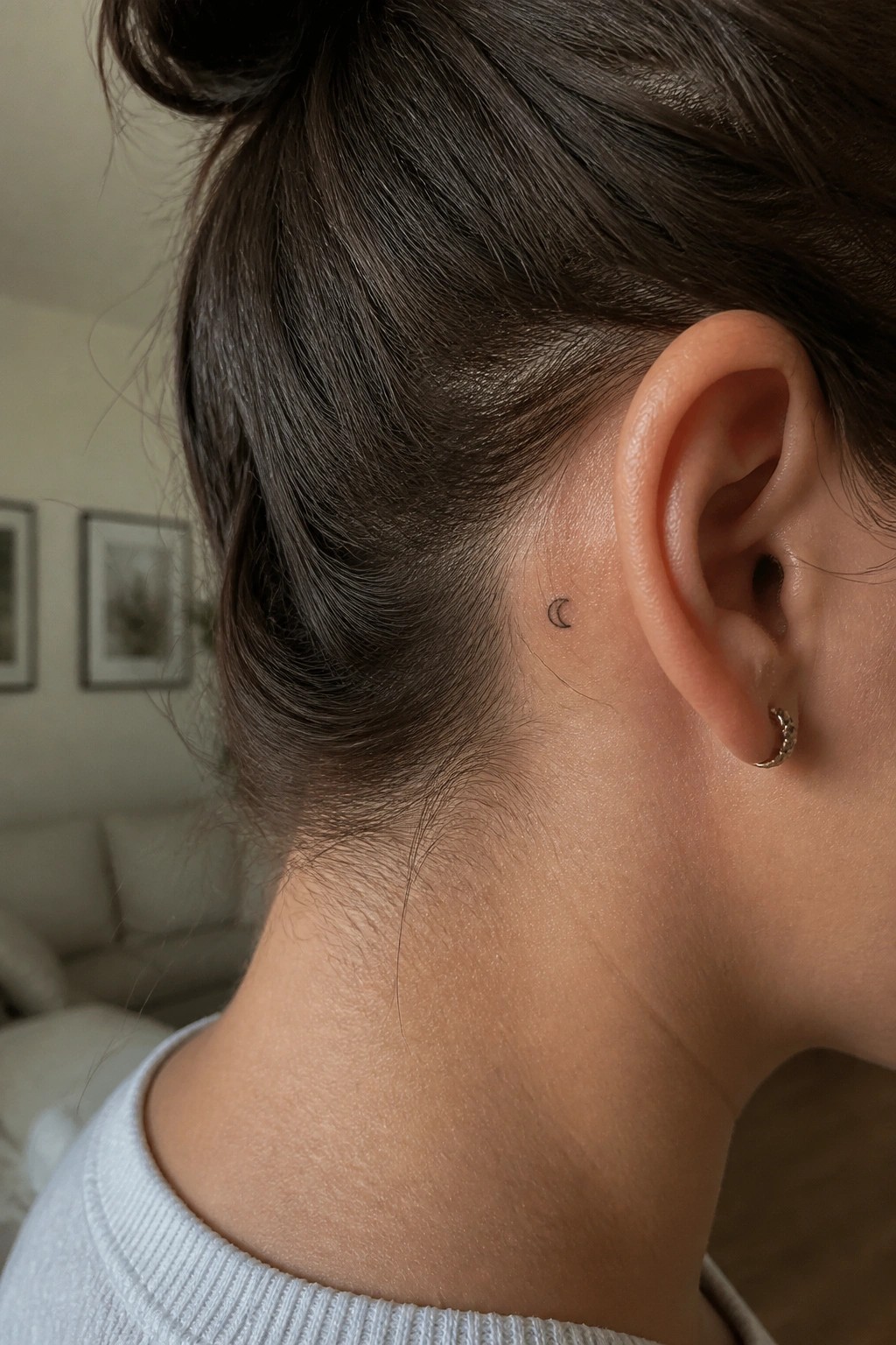 Woman with dark bun and crescent moon tattoo behind ear, gold hoop earring