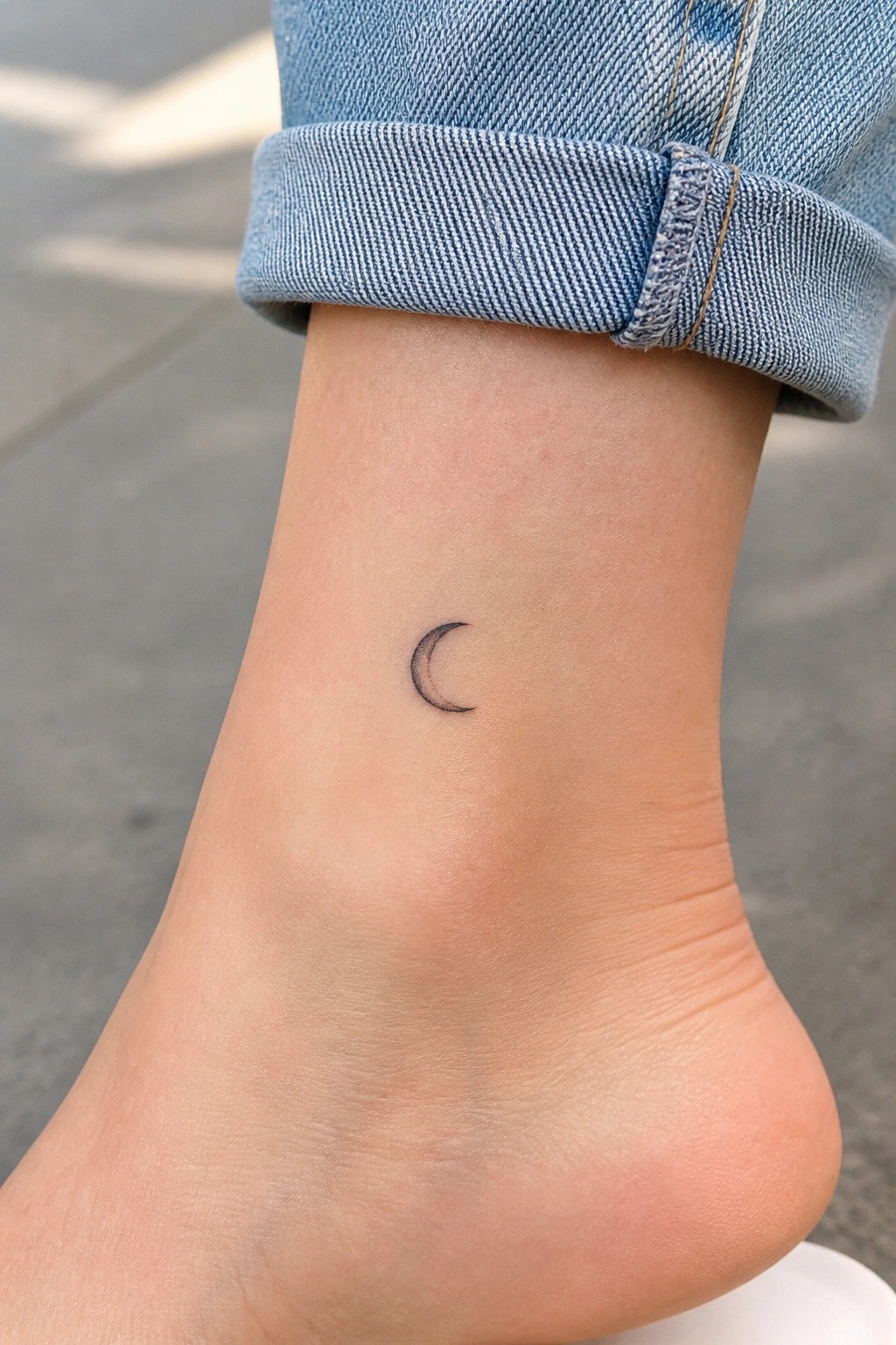 Small crescent moon tattoo on ankle below rolled blue denim cuff