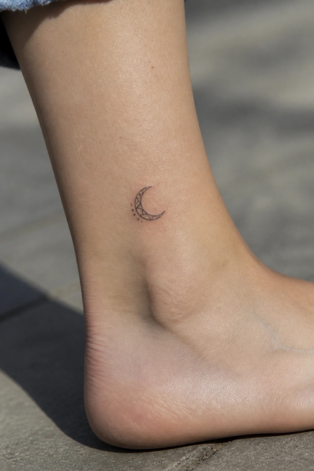 Small fine line crescent moon tattoo on the ankle with geometric shading and trailing dots
