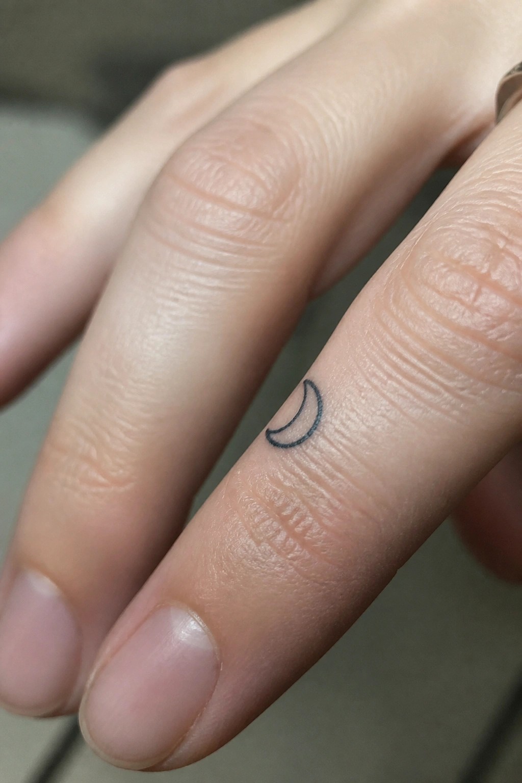 Close-up of light skin with a small black crescent moon tattoo on one finger.