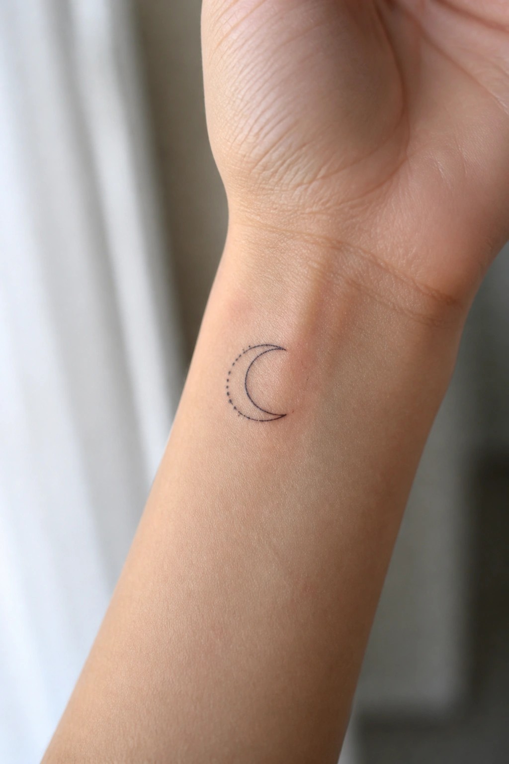 Small crescent moon tattoo with dotted edge on light-skinned wrist