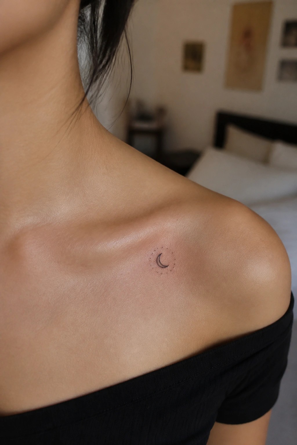 Close up of a small crescent moon tattoo with surrounding dots on a woman's upper shoulder.