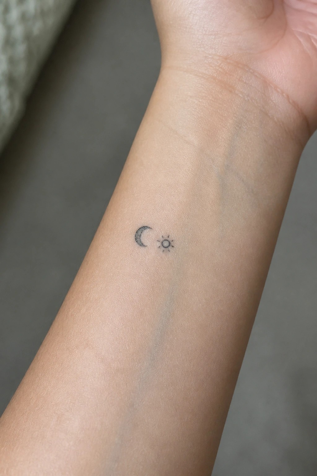 Small crescent moon and sun tattoo on light-skinned inner wrist