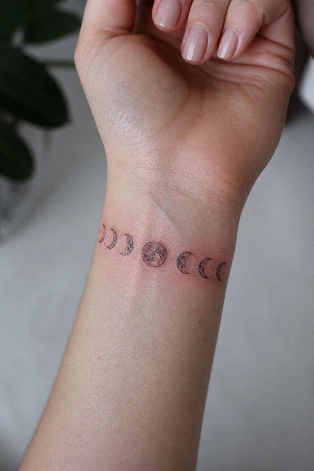 Small moon phase tattoo in a straight line across the inner wrist, showing the cycle from crescent to full moon in minimal black ink.