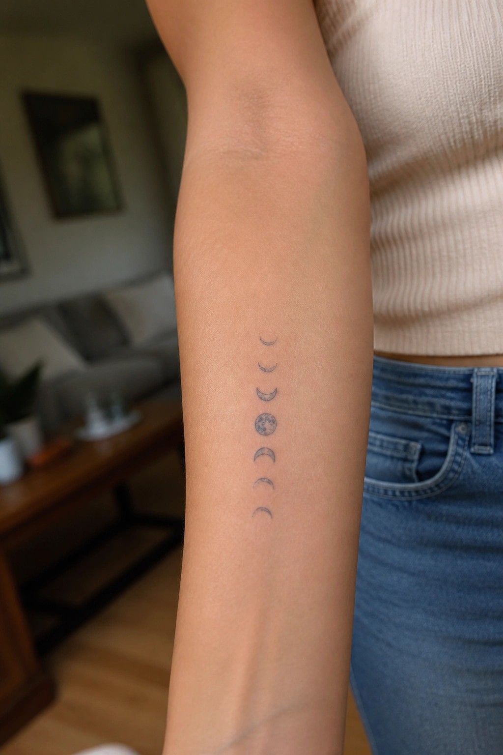 Fine line moon phases tattoo stacked vertically on the inner forearm in black ink.