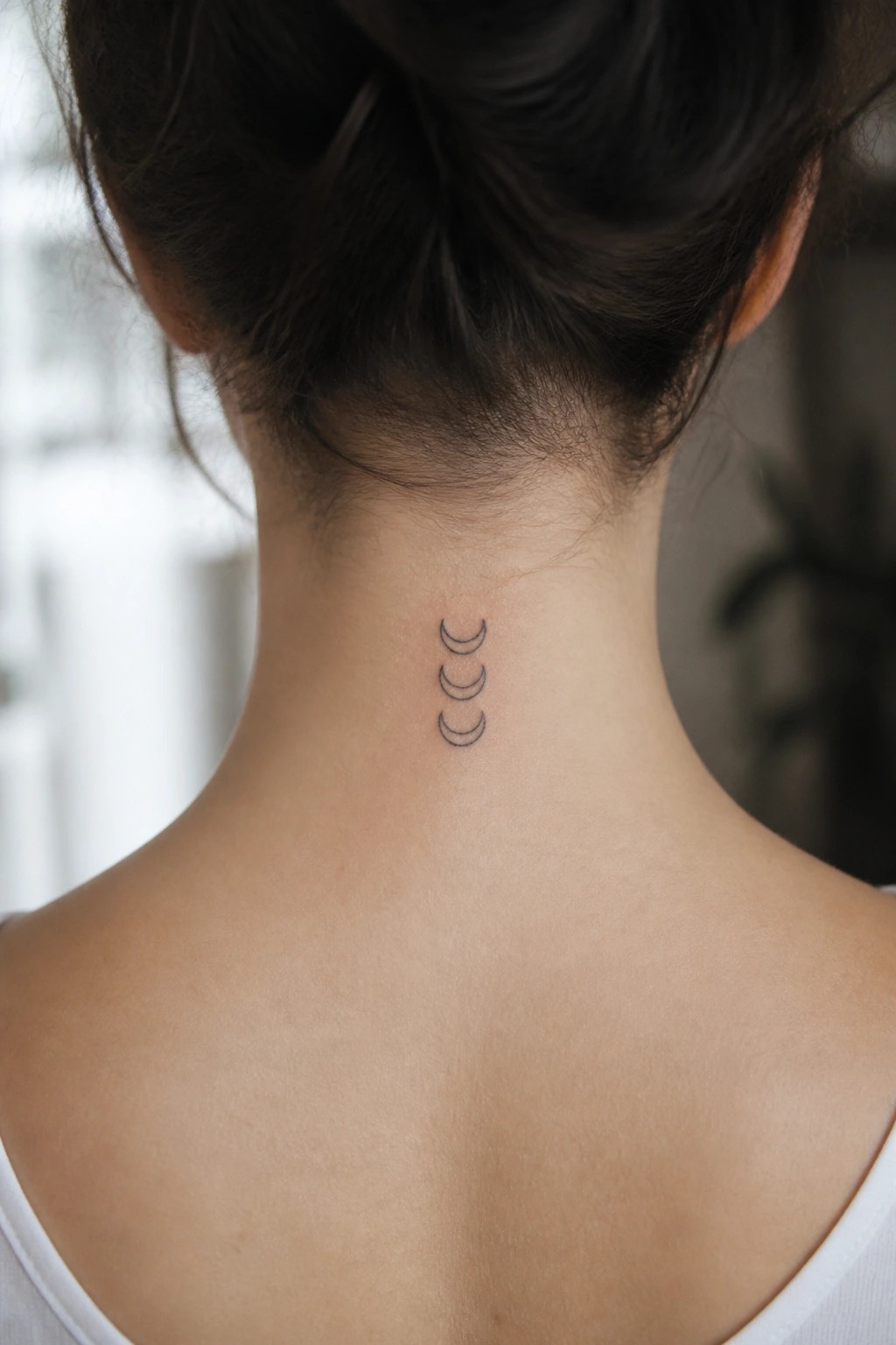Small tattoo of three crescent moons stacked vertically on the back of a woman's neck in thin black lines