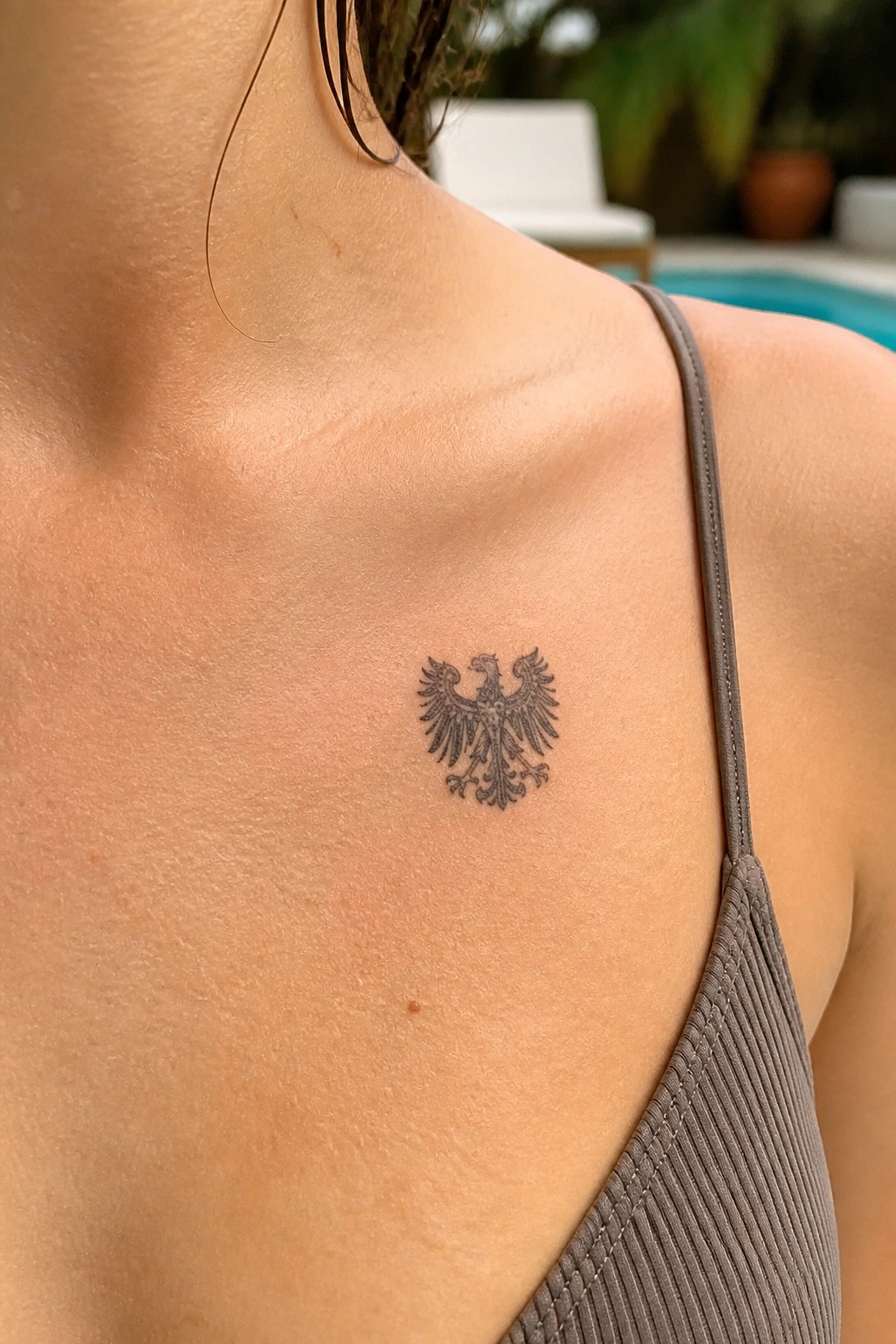 Double-headed eagle tattoo on shoulder above gray ribbed strap near pool
