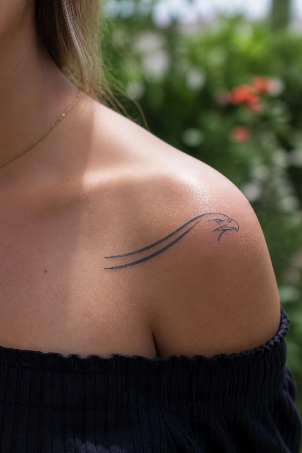 Minimalist line art eagle head tattoo on a woman's shoulder with trailing lines extending left