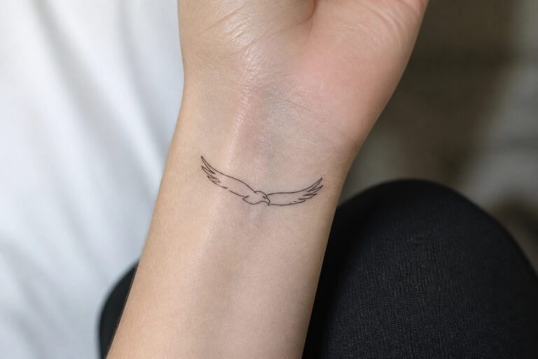 23 Minimalist Eagle Tattoo Ideas for Women Who Prefer Clean Designs Minimalist black line tattoo of a flying bird on inner wrist above blue jeans