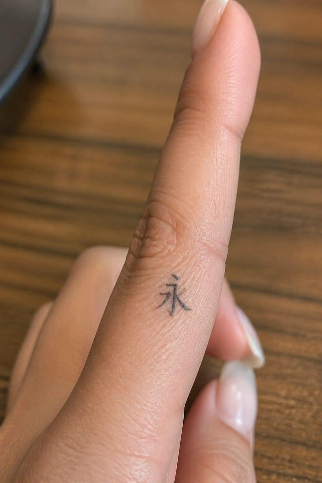 Small black Chinese character tattoo placed on the side of a finger