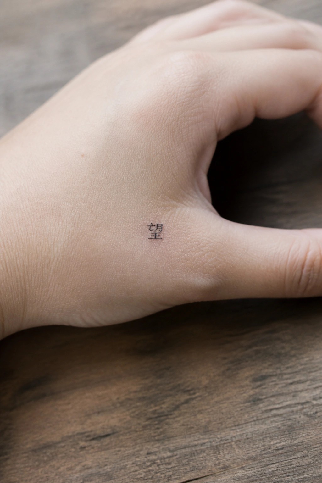 Small black Chinese character tattoo on the side of a hand near the thumb base