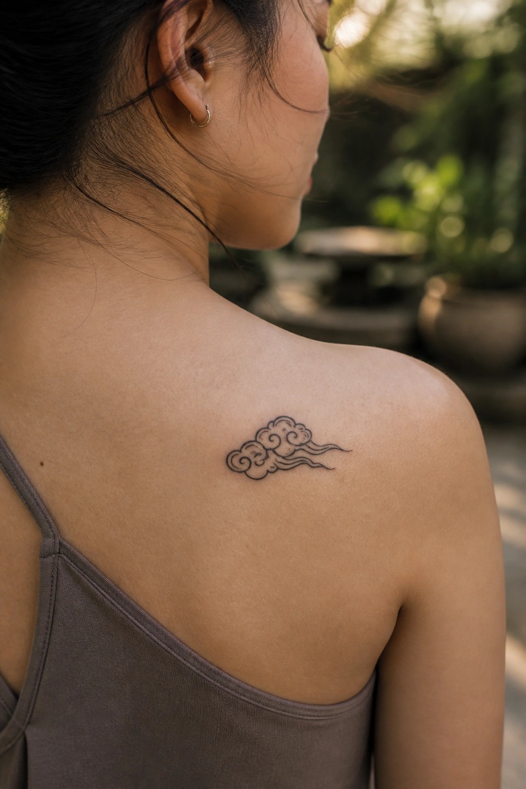 Small black line drawing of a traditional Chinese cloud tattoo on a woman's upper back near the shoulder blade