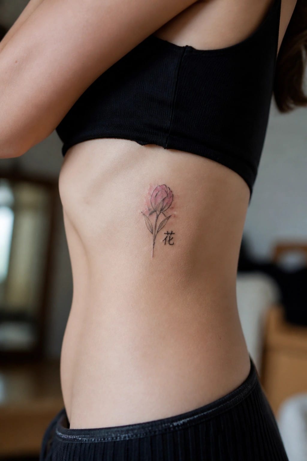 Pink flower tattoo with Chinese character on skin below black crop top