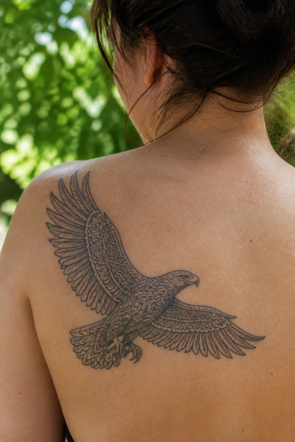 Black and grey eagle tattoo in flight across a woman's upper back and shoulder, with detailed wings spread wide.