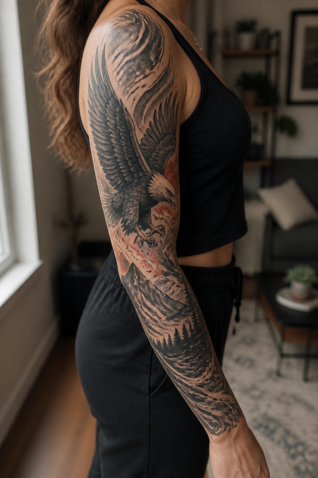 Woman showing a full sleeve tattoo of a soaring eagle above mountains and trees in black and grey with red accents