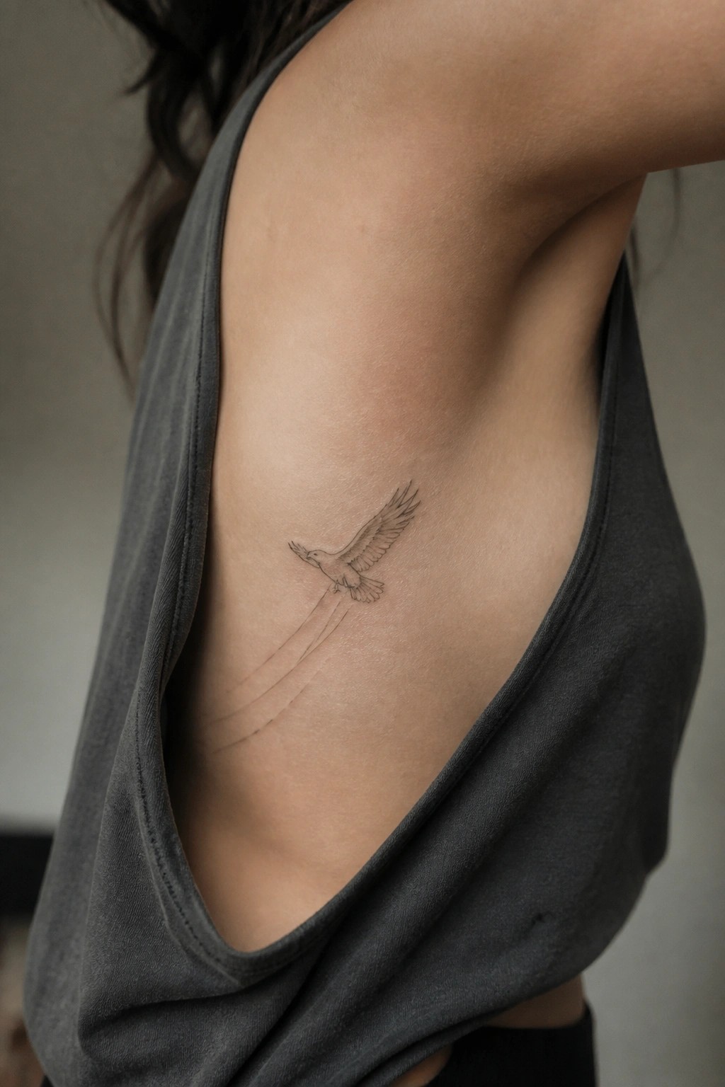 Minimalist line drawing of a small eagle in flight tattooed on the upper rib area with motion lines trailing behind it