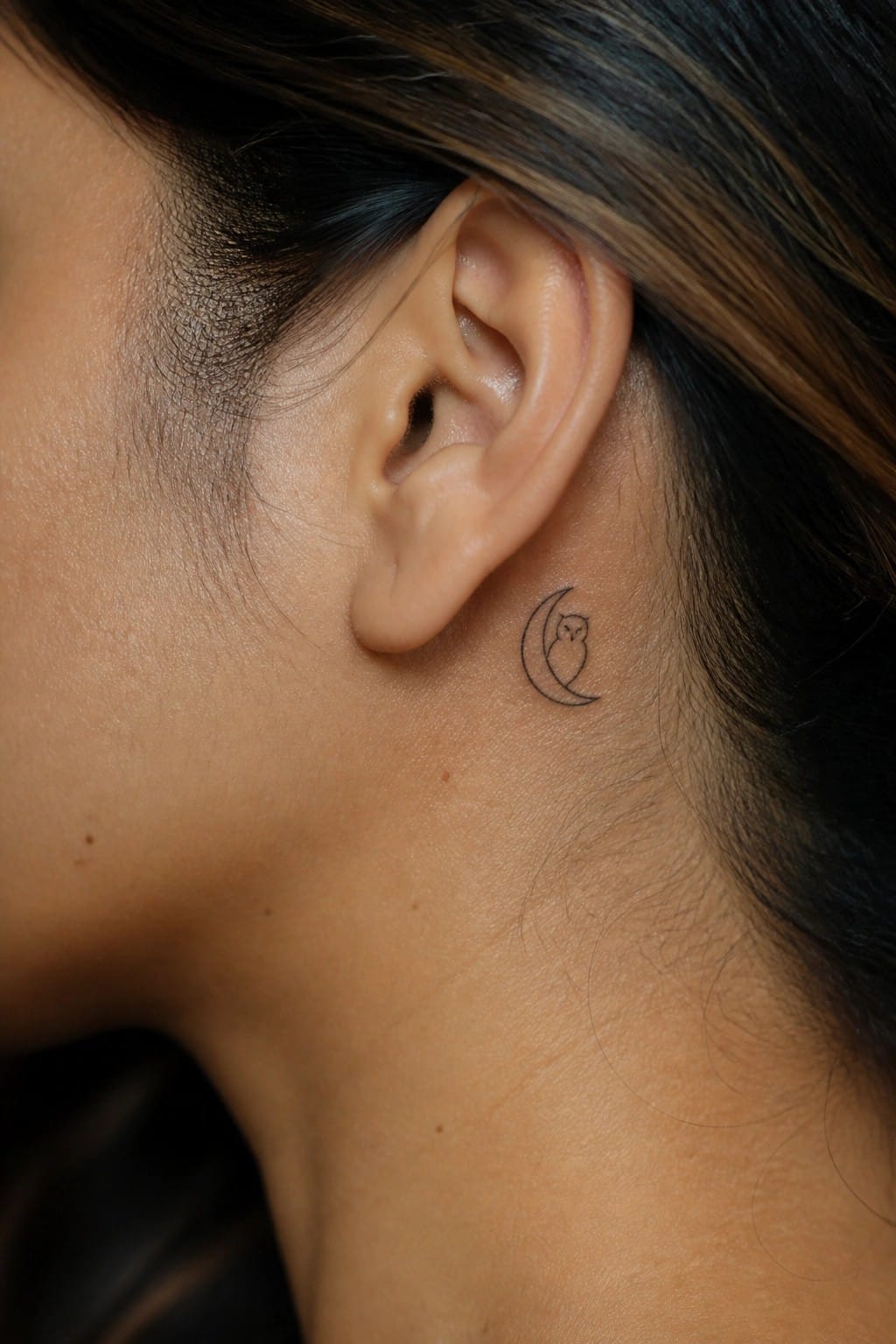 Close-up of ear with small crescent moon and owl tattoo behind it.