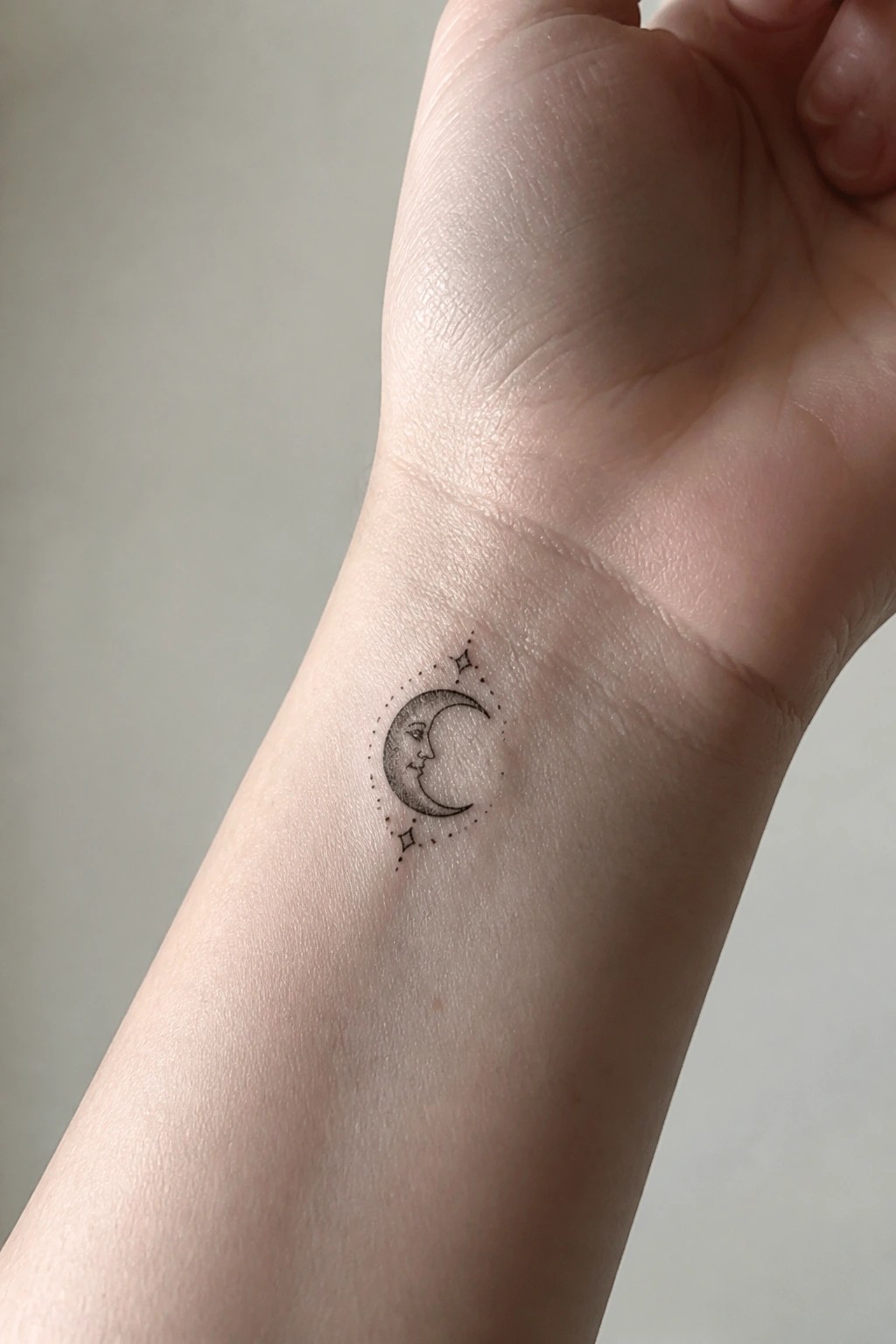 Delicate crescent moon face tattoo with stars on light-skinned wrist