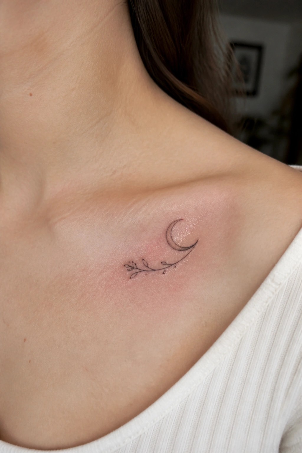 Crescent moon and leafy vine tattoo on reddened shoulder with white top