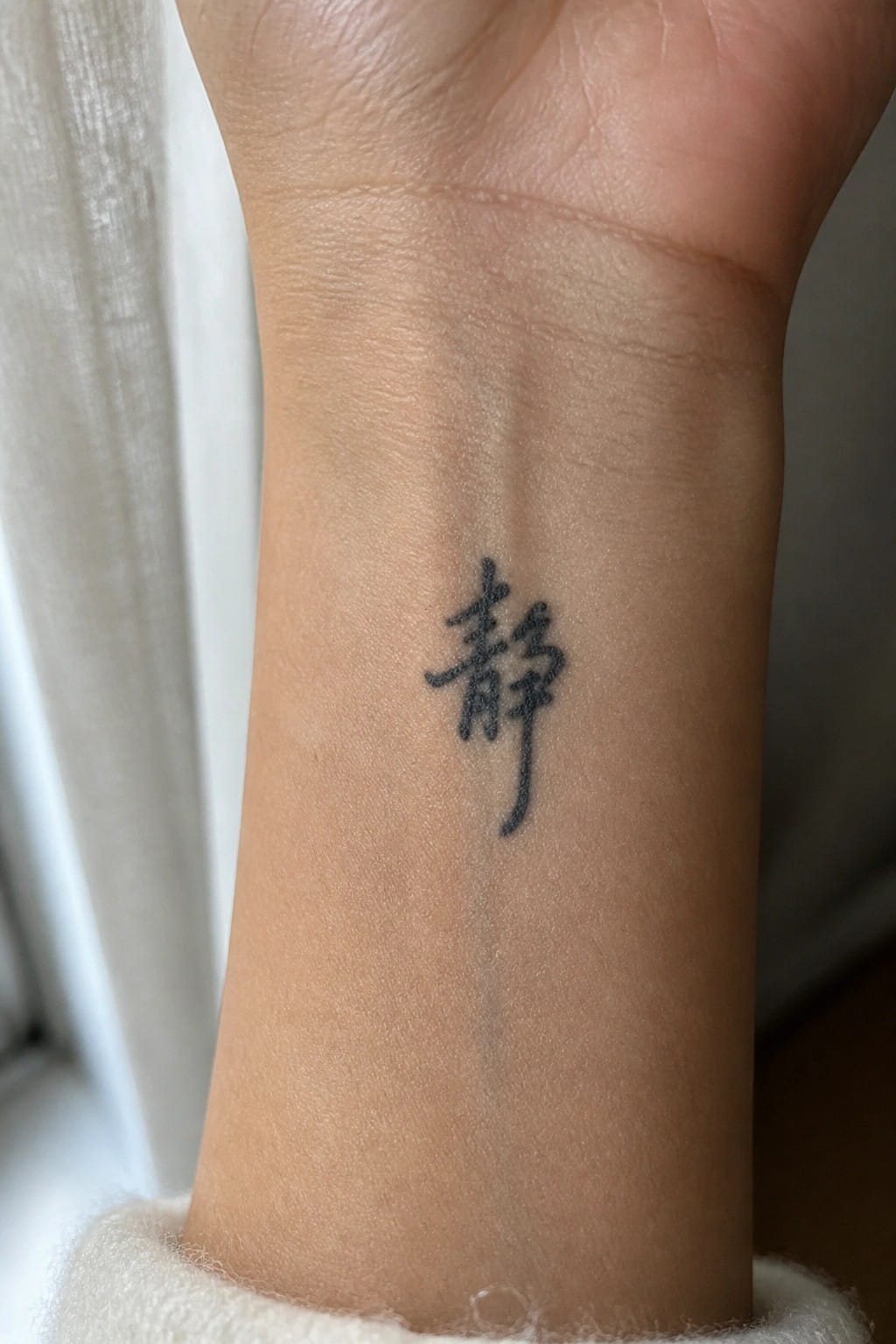 Small black Chinese character tattoo on the inner wrist in simple calligraphy style.