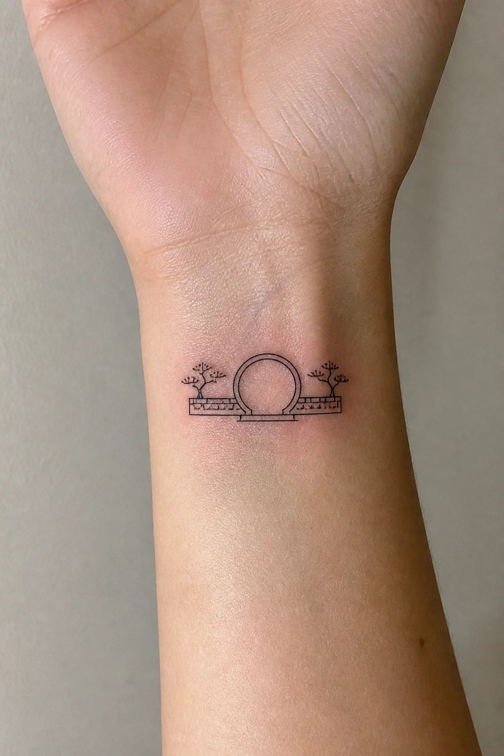 Minimalist black line tattoo of circular gate with trees on brick wall