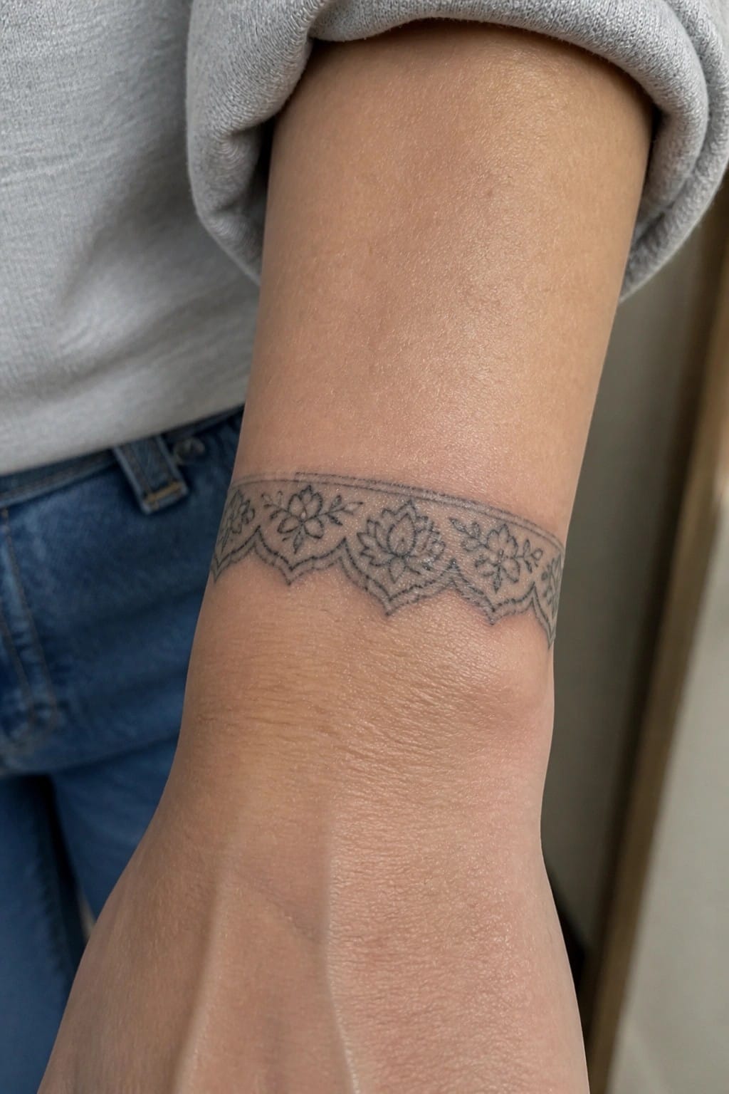 Wrist with black floral lace tattoo, gray sweatshirt sleeve, blue jeans visible