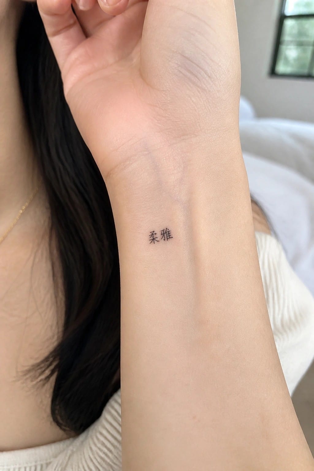 Raised arm showing small black Chinese characters tattoo on inner wrist