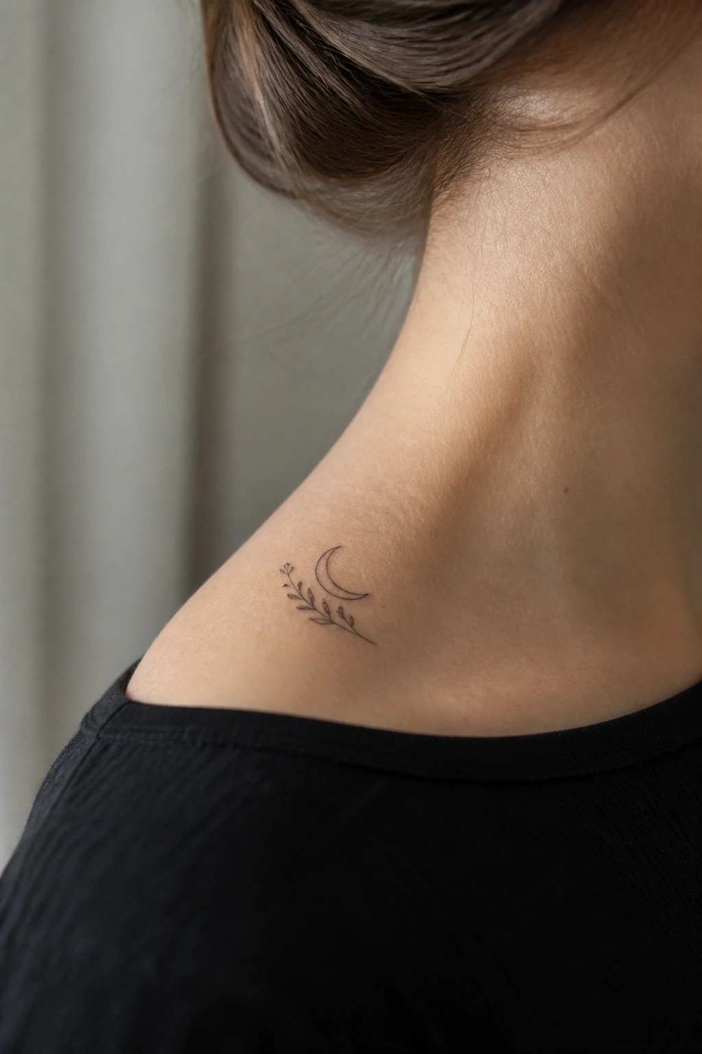 Crescent moon and leafy branch tattoo on neck above black top