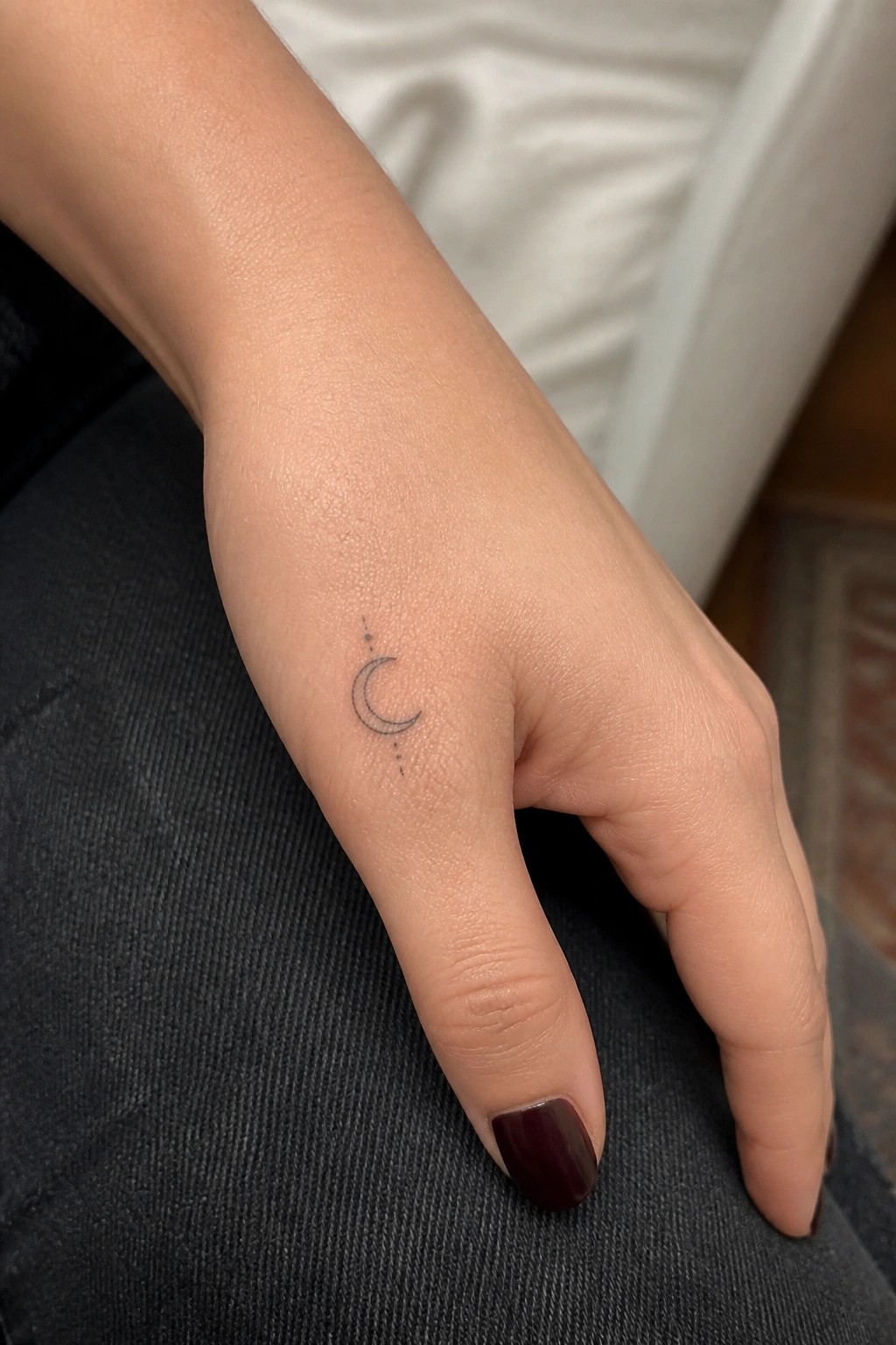 Crescent moon tattoo with dots on wrist near thumb with dark polish