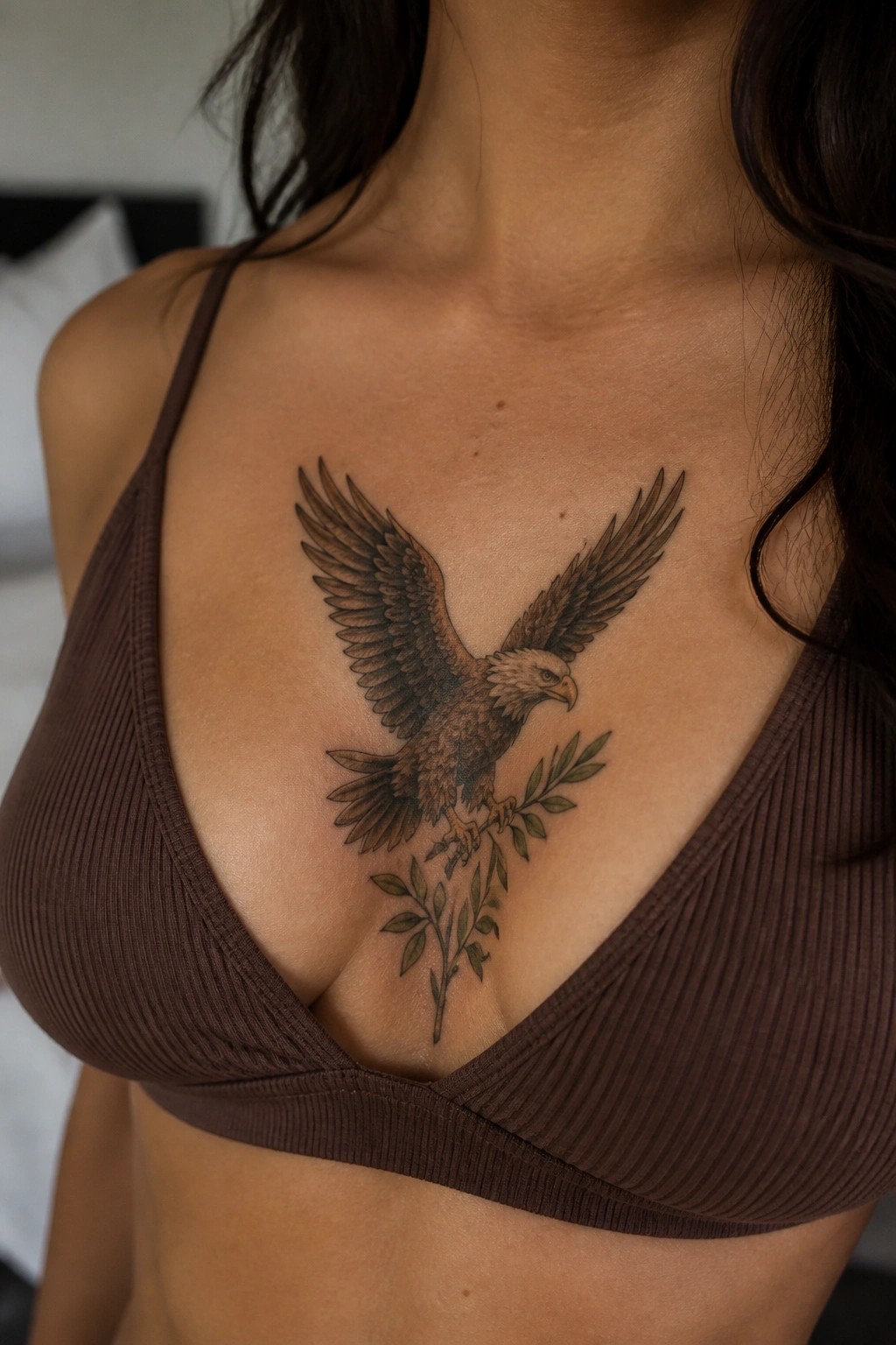 Woman's chest with large eagle and olive branch tattoo over brown ribbed bra
