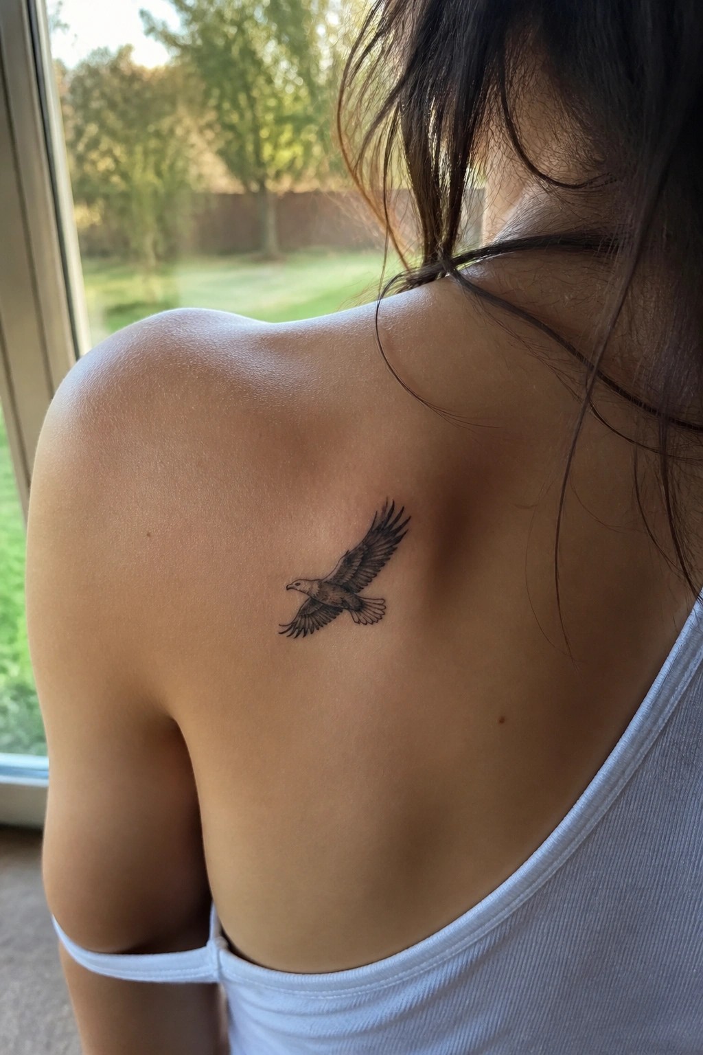 realistic black and grey eagle tattoo in flight on a woman's upper back near the shoulder blade