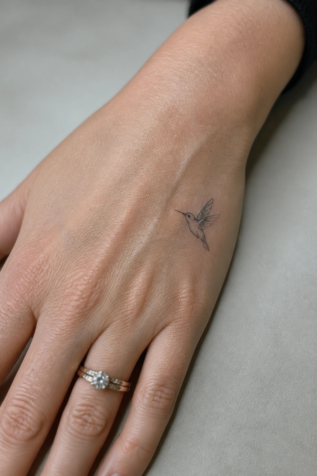 Fine line hummingbird tattoo placed on the side of the hand above the ring finger