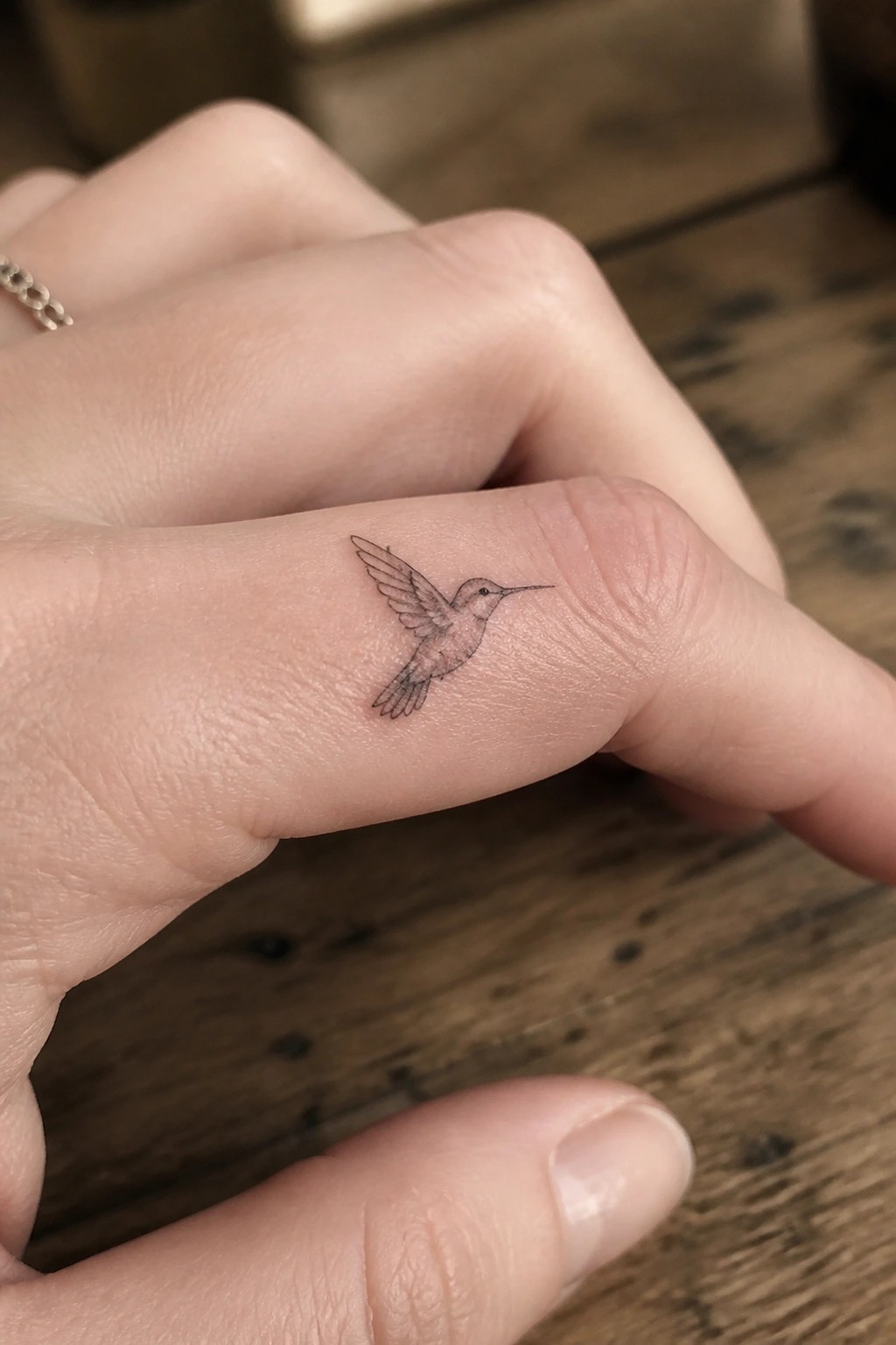 Fine line hummingbird tattoo on the side of a finger