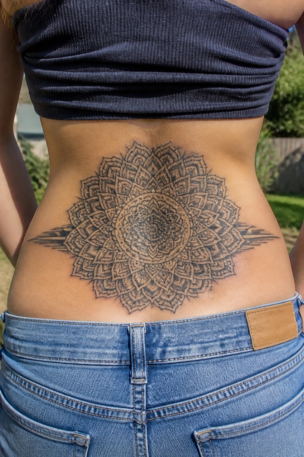 Large mandala tattoo on lower back between dark crop top and jeans