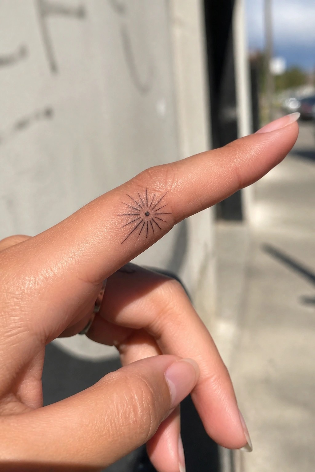 Index finger with black sunburst tattoo and silver ring on adjacent finger