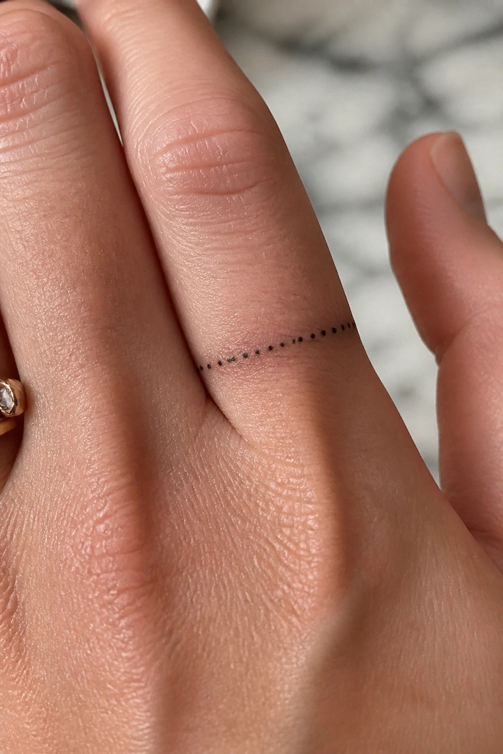 Close-up of a thin dotted line tattoo placed along the side of a finger