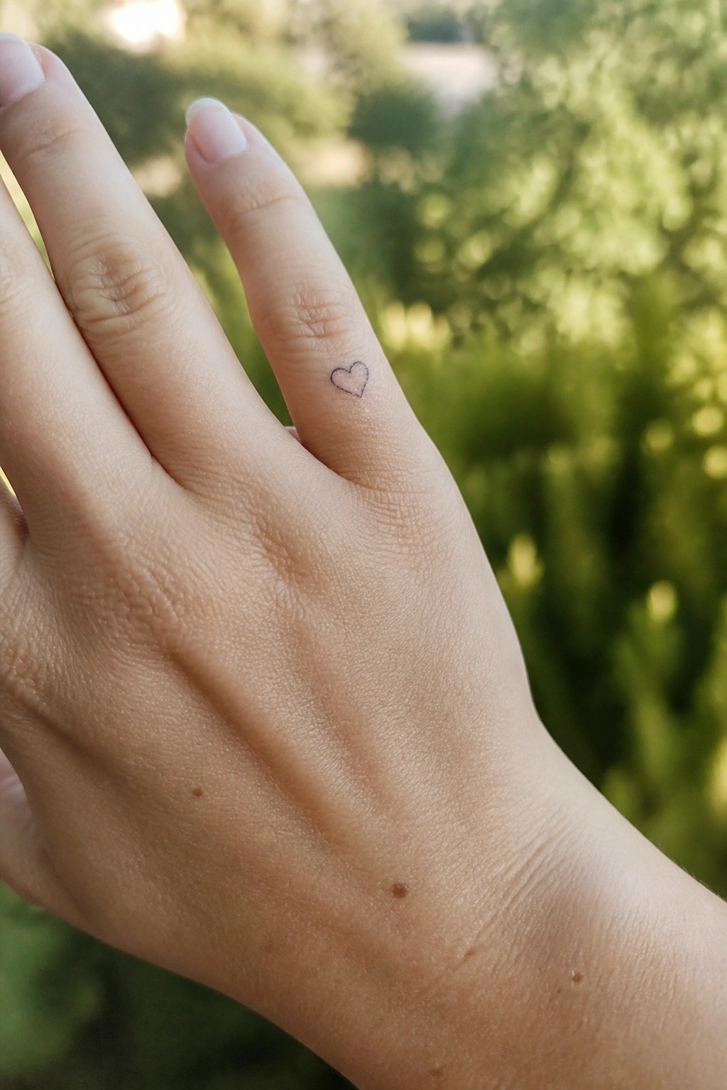 Close up of a tiny heart outline tattoo on the side of a finger