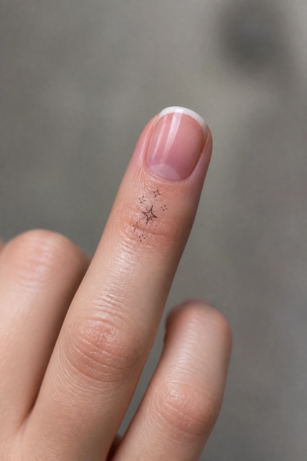 Finger with French manicure and small black star tattoo near cuticle