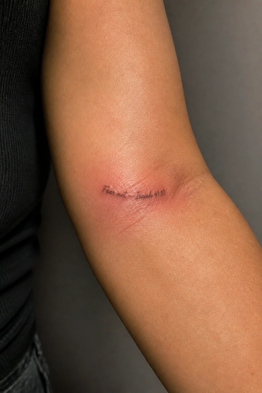 Small cursive tattoo reading Fear not Isaiah 41:10 on the inner forearm with light redness around the fresh ink.
