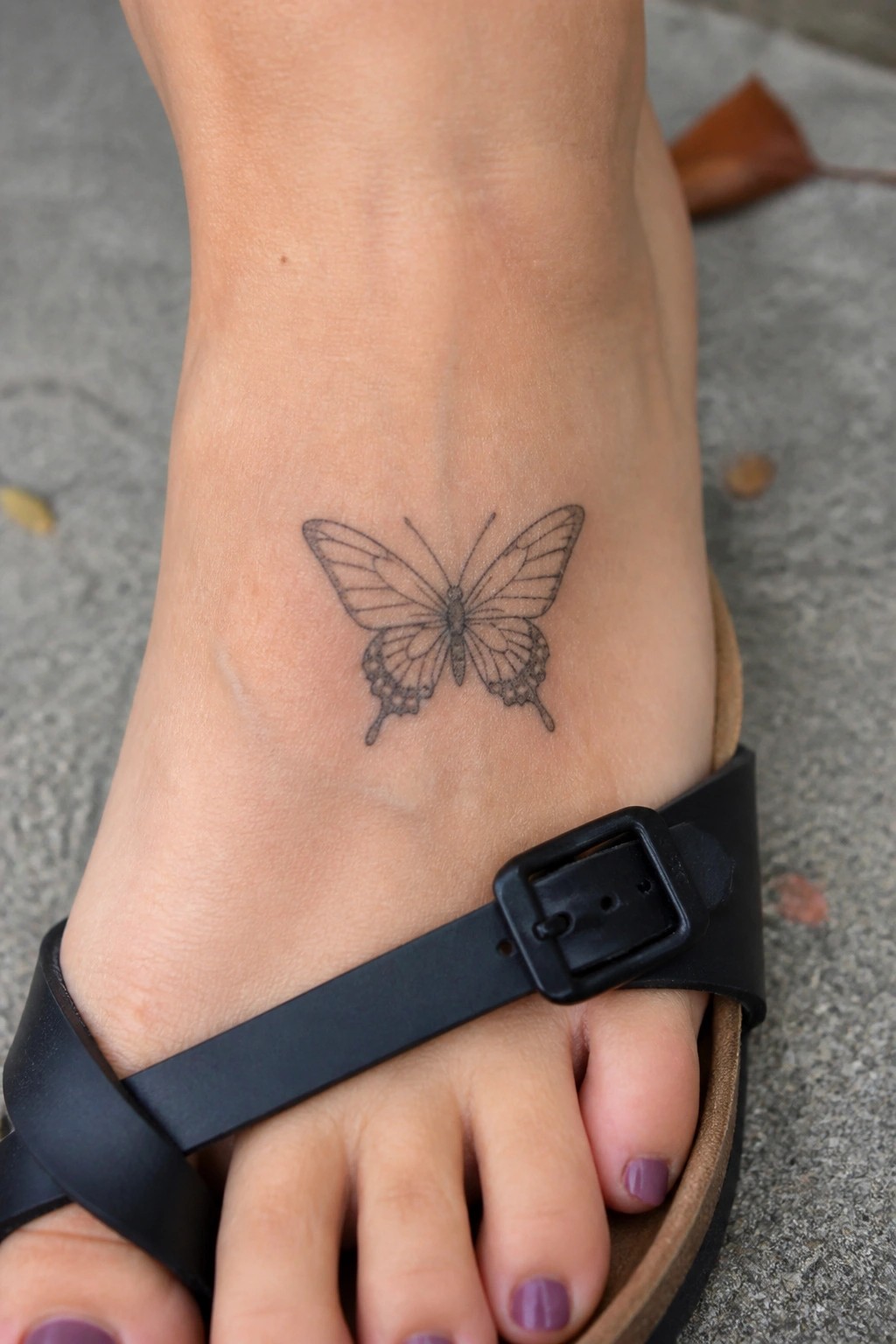 Fine line butterfly tattoo on the top of a foot in a black sandal