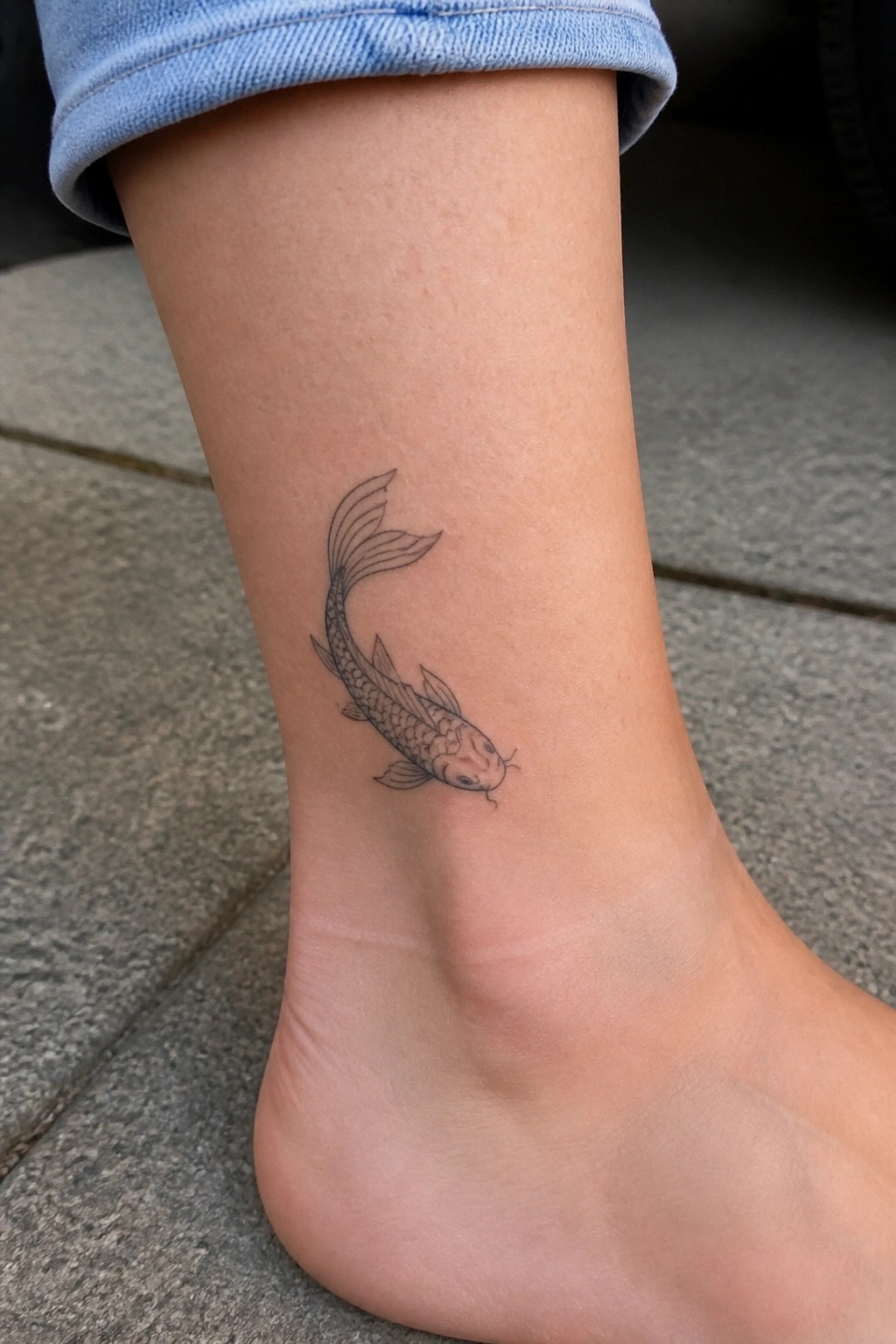 Koi fish tattoo on ankle above bare foot with rolled blue jeans