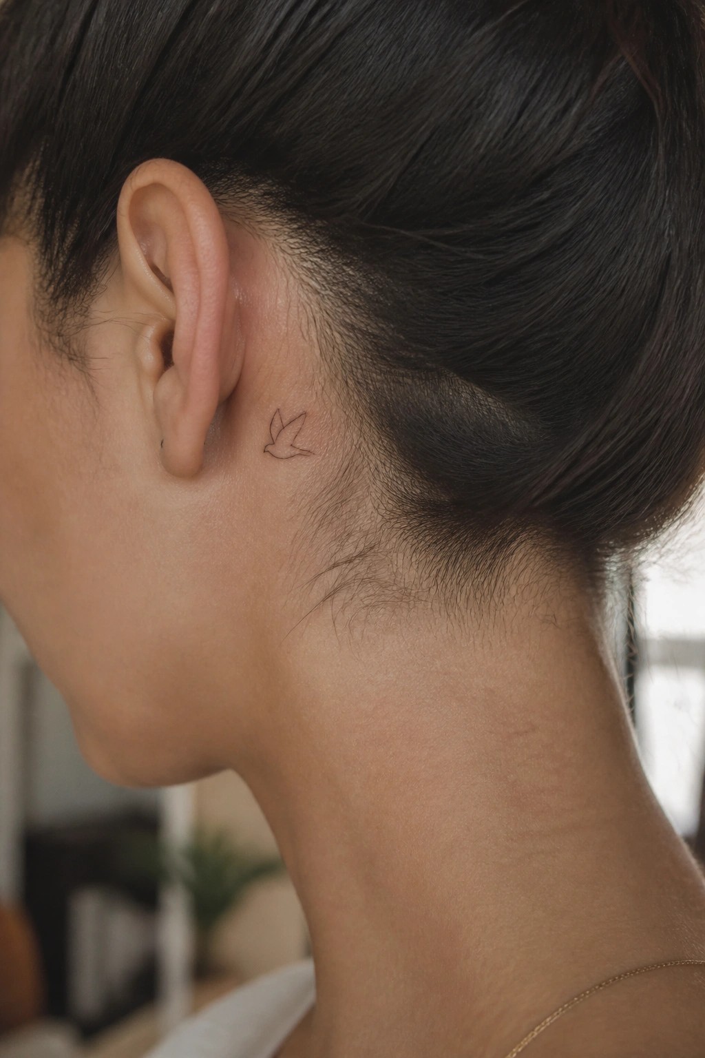 Small fine line bird tattoo placed behind the ear on the side of the neck