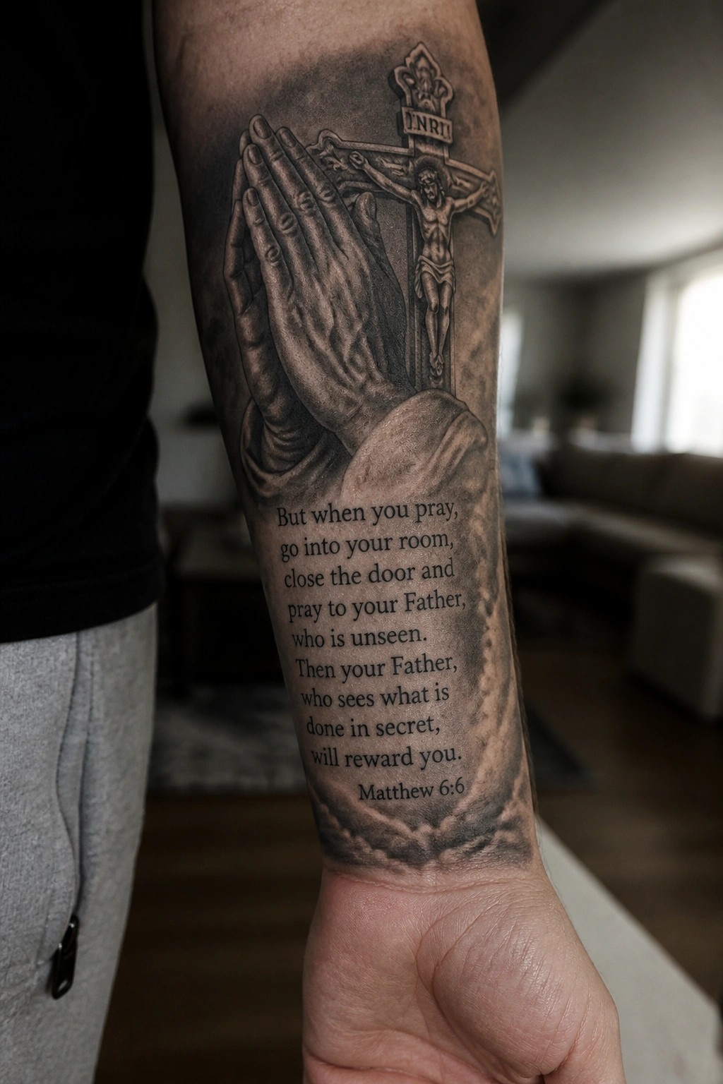 Black and gray forearm tattoo of praying hands, crucifix, and Matthew 6:6 verse