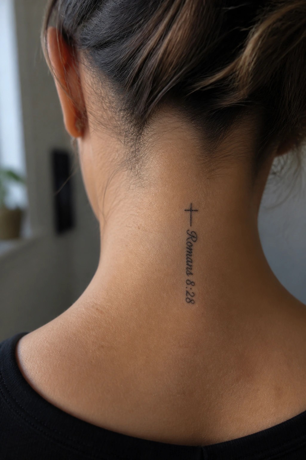 Neck tattoo of cross above Romana 8:28 text on light skin with black top.