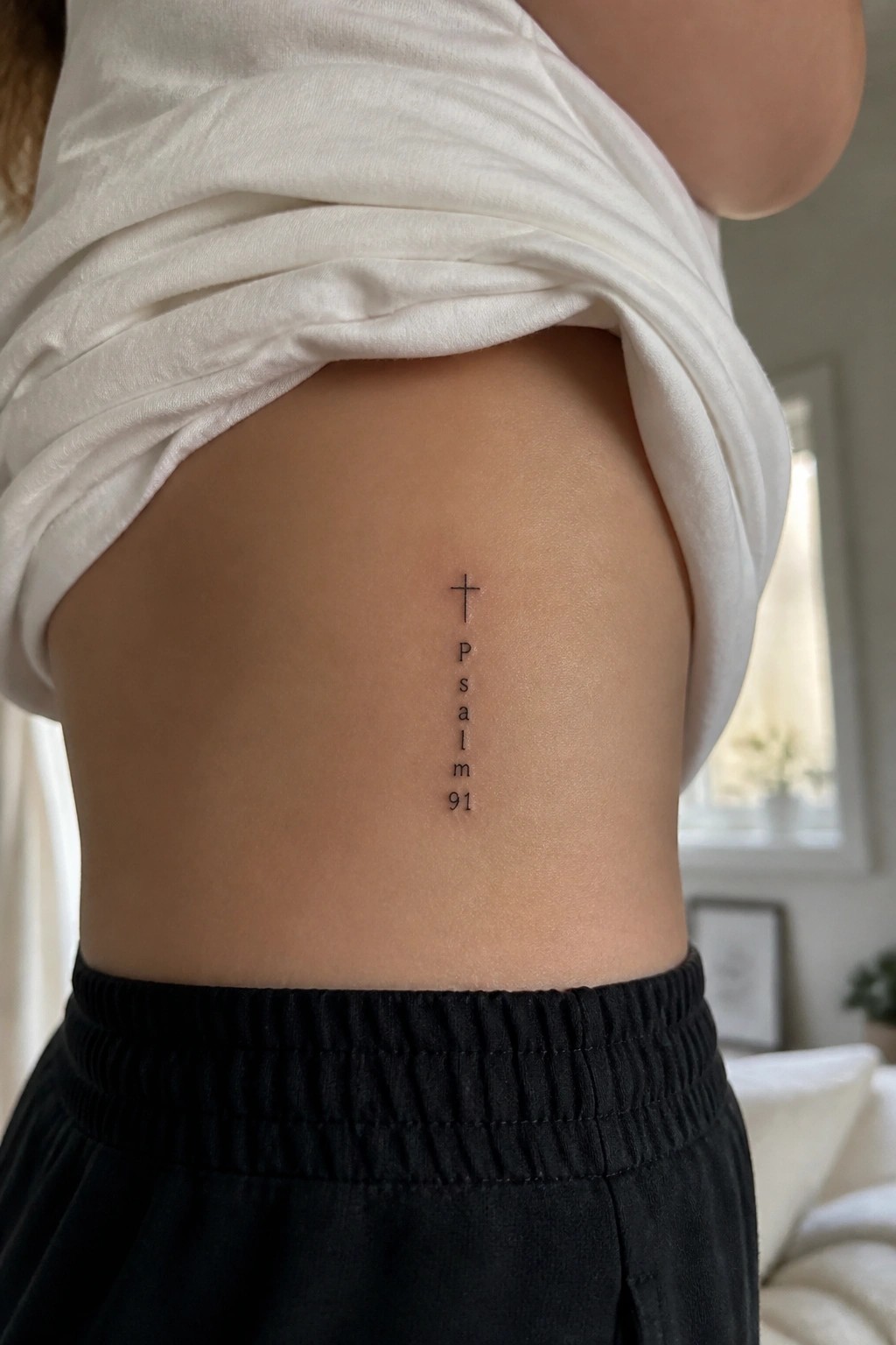 Person lifting white shirt to show vertical Psalm 91 cross tattoo on side.