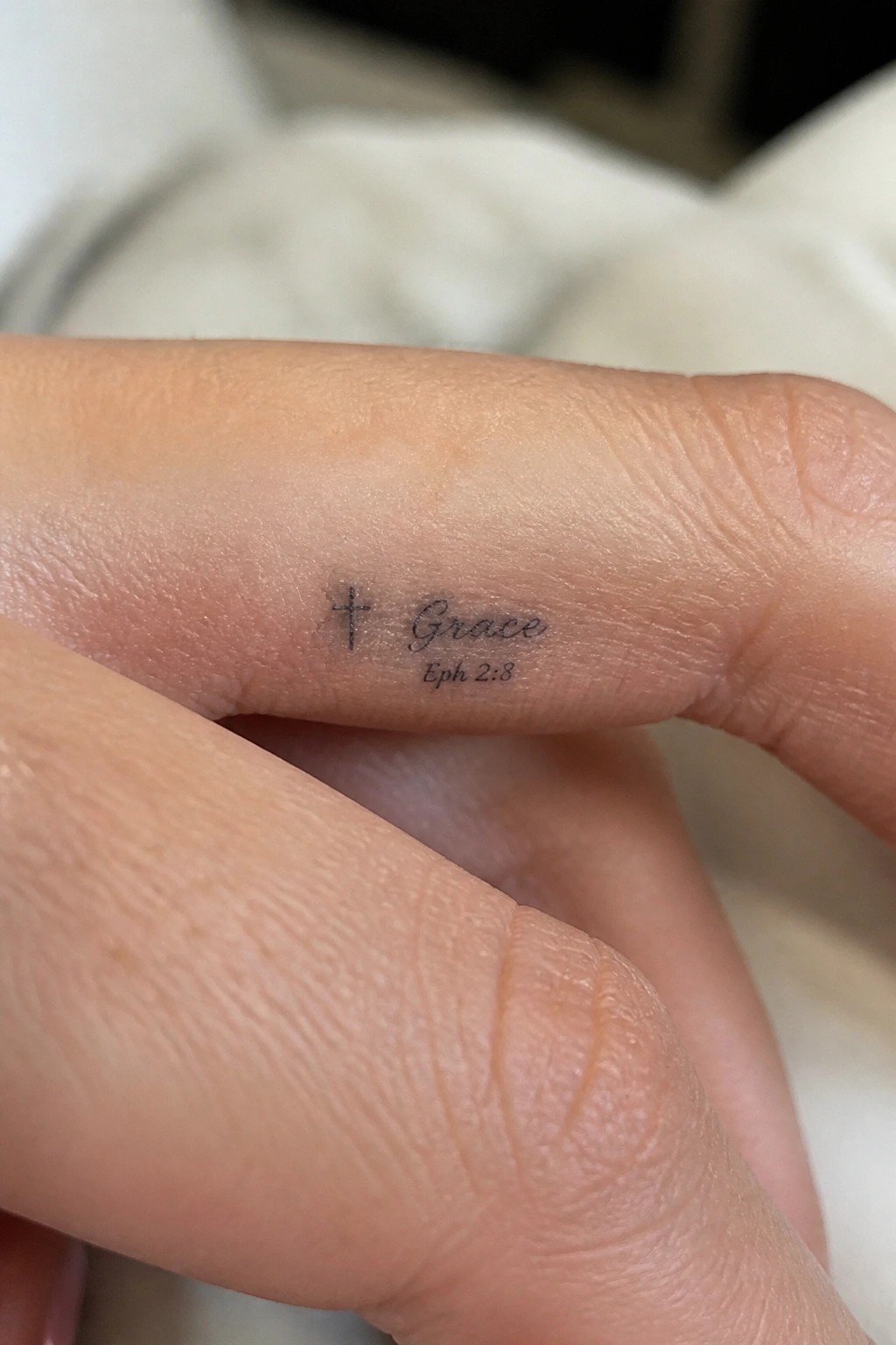 Small cross with the word grace and eph 2 8 on the side of a finger